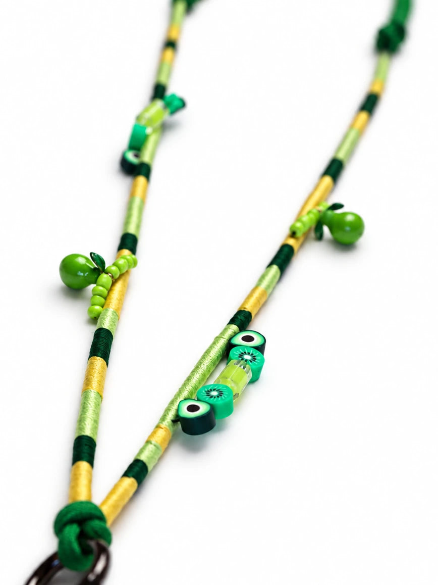 Close-up of kiwi slice and avocado beads on the green and gold wrapped cord of the Amalfi phone strap